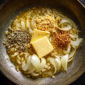 Onions sautéing in butter or ghee with mustard seeds and spices being added.