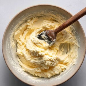 A bowl of cream cheese dough being mixed with a wooden spoon, showcasing the soft, smooth texture of the dough.