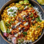 A Street Corn Chicken Rice Bowl with grilled chicken, roasted corn, avocado, lime wedge, and cilantro over white rice, drizzled with creamy sauce.