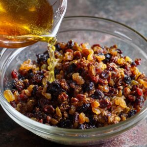 A bowl of mixed dried fruits and raisins being soaked with melted butter or rum poured over them.