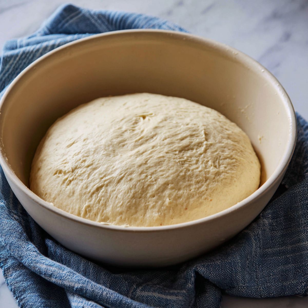 Stollen dough resting and rising in a bowl covered with a blue cloth.