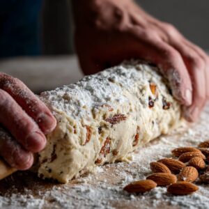 Hands shaping a dough log filled with almonds and raisins on a floured surface.