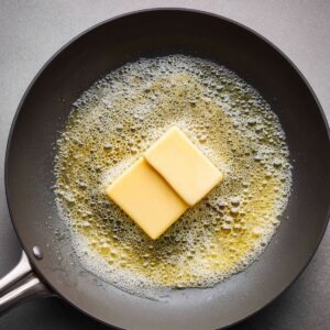 A large cube of butter is placed in a hot skillet, starting to melt and bubble, indicating the preparation of a flavorful cooking base for the fish.