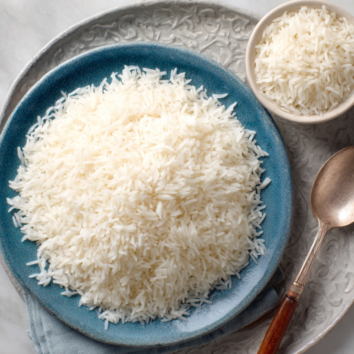 A simple plate of fluffy white basmati rice, served with a spoon, looking like plain rice or the base for a more complex dish.
