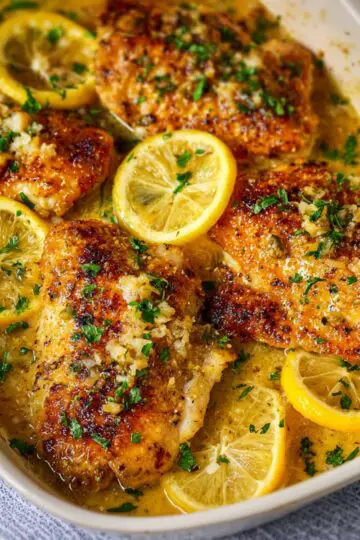 Baked Lemon Butter Chicken Golden baked chicken thighs simmering in a creamy lemon-butter sauce, topped with fresh parsley and surrounded by bright lemon slices.