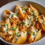 A white dish filled with Buffalo Chicken Stuffed Shells Recipe shells, topped with melted cheese, crumbled blue cheese, and chopped green onions for garnish.
