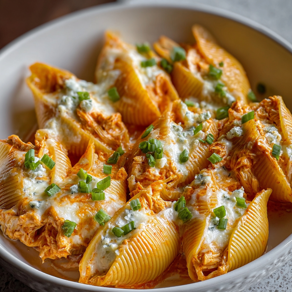 A white dish filled with Buffalo Chicken Stuffed Shells Recipe shells, topped with melted cheese, crumbled blue cheese, and chopped green onions for garnish.