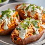 Buffalo Chicken Stuffed Sweet Potatoes served on a plate, topped with creamy ranch dressing, crumbled blue cheese, and chopped green onions.