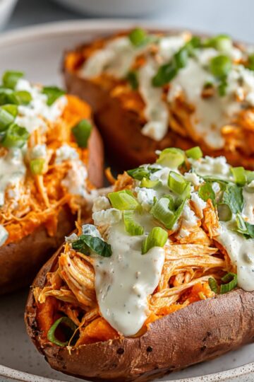 Buffalo Chicken Stuffed Sweet Potatoes served on a plate, topped with creamy ranch dressing, crumbled blue cheese, and chopped green onions.