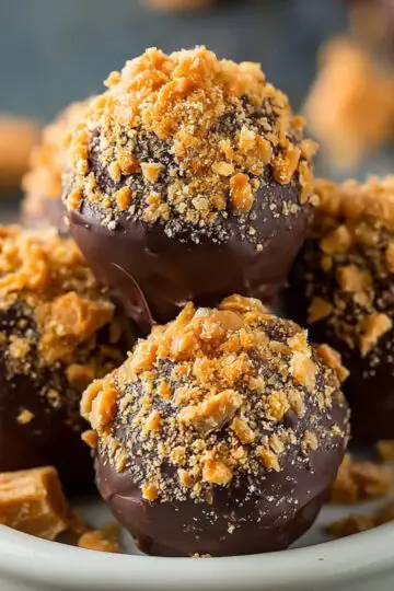 Close-up of Butterfinger Balls truffles topped with golden crushed candy bits, neatly arranged in a small white bowl.
