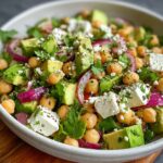 Chickpea Feta Avocado Salad A plate featuring sliced avocado, chickpeas, cherry tomatoes, red onion, crumbled feta cheese, and fresh herbs.