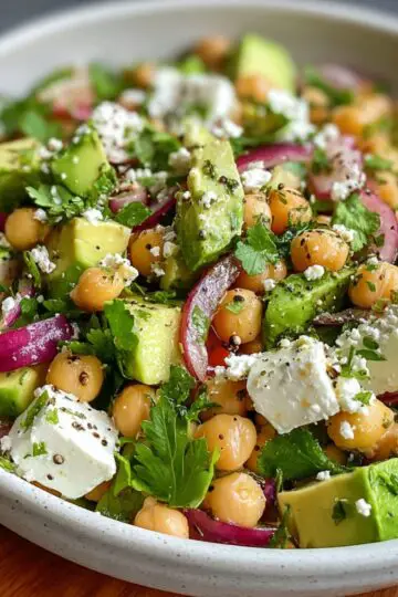 Chickpea Feta Avocado Salad A plate featuring sliced avocado, chickpeas, cherry tomatoes, red onion, crumbled feta cheese, and fresh herbs.