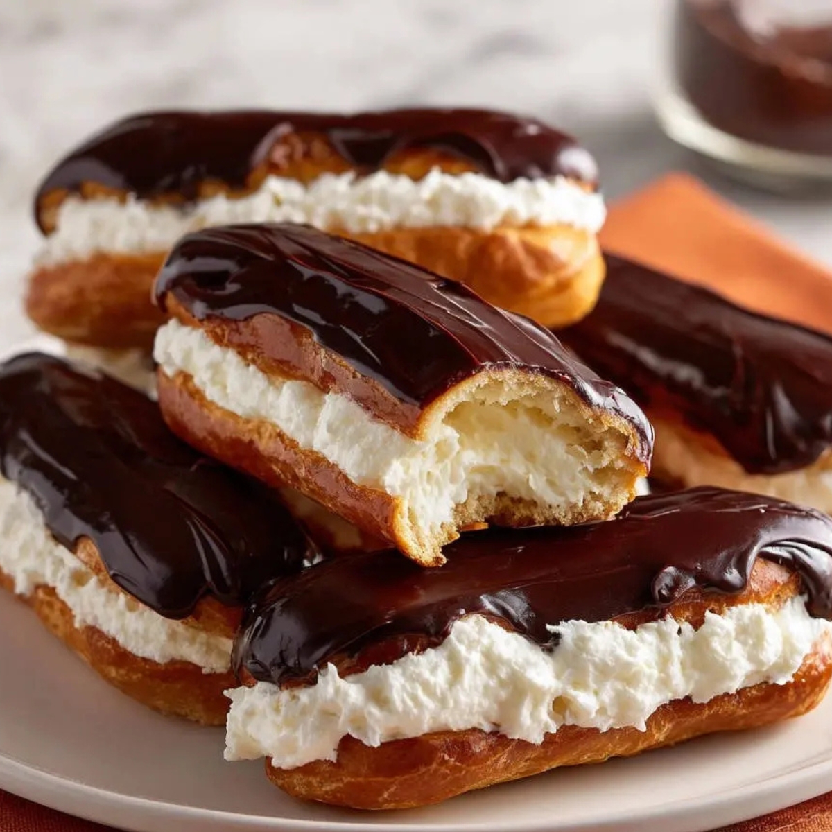 The Best Chocolate Eclairs Recipe In 3 steps 9 Chocolate Eclairs Plate of chocolate éclairs filled with cream, one with a bite taken out to show the airy interior, topped with rich glossy ganache.”