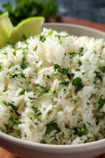 Cilantro Lime Rice A close-up bowl of cilantro lime rice, garnished with fresh cilantro and served with lime wedges on the side.