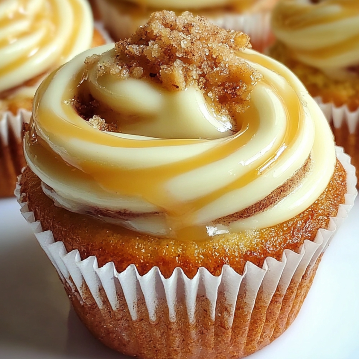 Cinnamon Roll Cupcakes topped with cream cheese frosting, brown sugar crumble, and a drizzle of caramel sauce.
