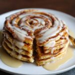 Slice cut from a stack of cinnamon roll pancakes showing the cinnamon swirl inside, topped with dripping glaze.