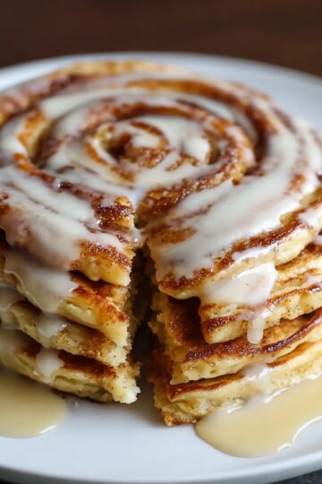 Slice cut from a stack of cinnamon roll pancakes showing the cinnamon swirl inside, topped with dripping glaze.