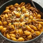 Creamy Beef And Shells Bowl of creamy beef and shells pasta topped with shredded cheese and parsley, with a spoon on the side.