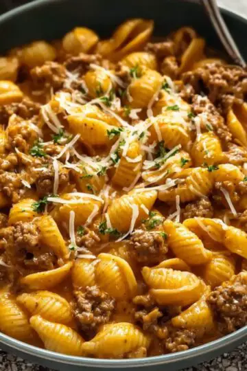 Creamy Beef And Shells Bowl of creamy beef and shells pasta topped with shredded cheese and parsley, with a spoon on the side.