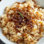 French Onion Butter Rice A white bowl of French onion butter rice, featuring a mound of caramelized onions in the center and a spoon to the side.