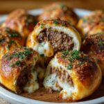 Garlic Parmesan Cheeseburger Bombs A plate of baked garlic Parmesan cheeseburger bombs, one opened to show melty cheese and beef filling, topped with crispy Parmesan and chopped herbs.