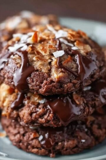 Plate of German chocolate cookies drizzled with chocolate and topped with golden toasted coconut flakes, set on a warm-toned tablecloth.