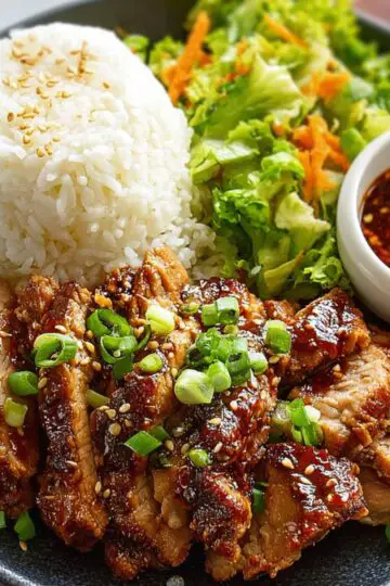 Korean BBQ pork A full Korean BBQ meal plate featuring sliced marinated pork, white rice, fresh salad, and a small bowl of dipping sauce topped with sesame seeds and chili flakes.