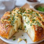 A cheesy Korean Cream Cheese Garlic Bread on a plate, golden brown and garnished with herbs, with dipping bowls in the background.