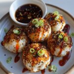 Korean Rice Balls drizzled with spicy sauce and garnished with sesame seeds and sliced green onions, served with a side of soy dipping sauce.