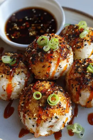 Korean Rice Balls drizzled with spicy sauce and garnished with sesame seeds and sliced green onions, served with a side of soy dipping sauce.