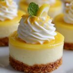 Mini lemon cheesecakes topped with whipped cream, lemon zest, and a small lemon slice on a white plate, showing creamy texture and crisp crust.