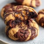 Peanut Butter Brownie Swirl Cookies A chocolate-and-peanut-butter swirl cookie broken open to reveal a gooey caramel-like peanut-butter center. The cookie has a soft, marbled texture.