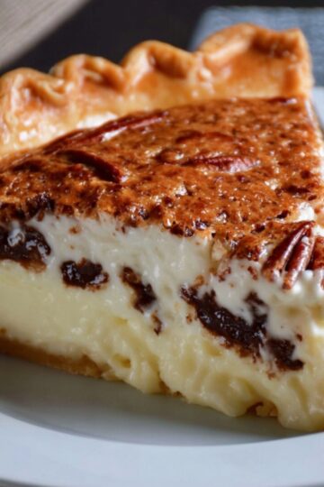 Possum Pie A close-up slice of creamy possum pie on a white plate, featuring a thick pecan-topped layer, rich chocolate swirls, and a smooth white cream filling inside a golden flaky crust. A fork rests beside the slice.