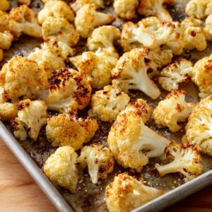 Roasted cauliflower florets on a baking sheet, golden and crispy with a light coating of seasoning and oil.