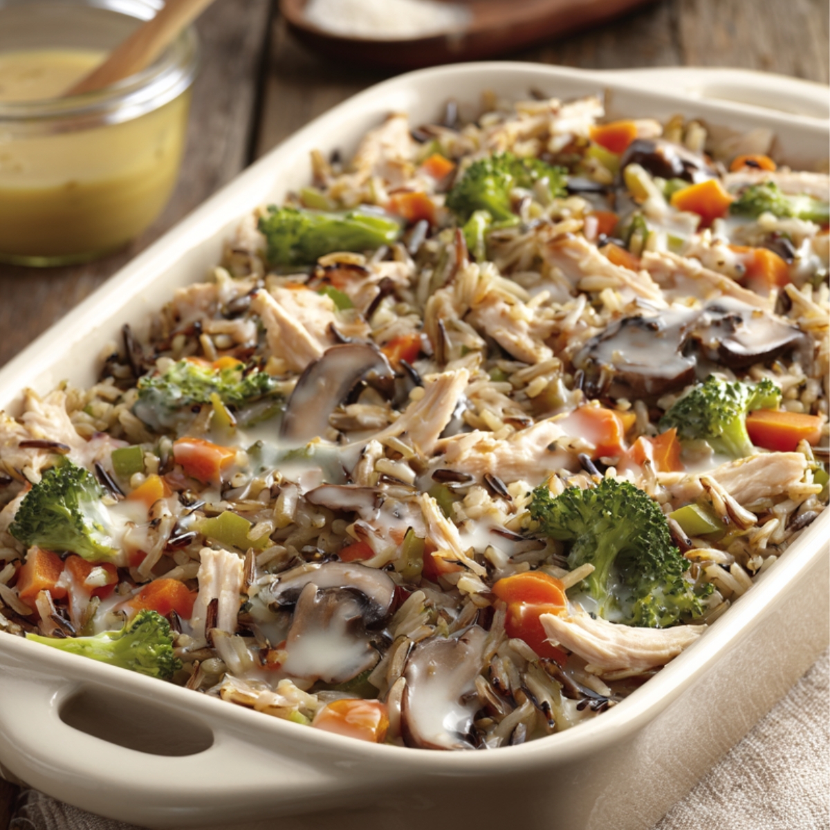 Delicious Chicken Wild Rice Casserole Recipe 12 "Bowl of creamy wild rice chicken casserole with mushrooms and herbs, with a spoon lifting a cheesy bite."