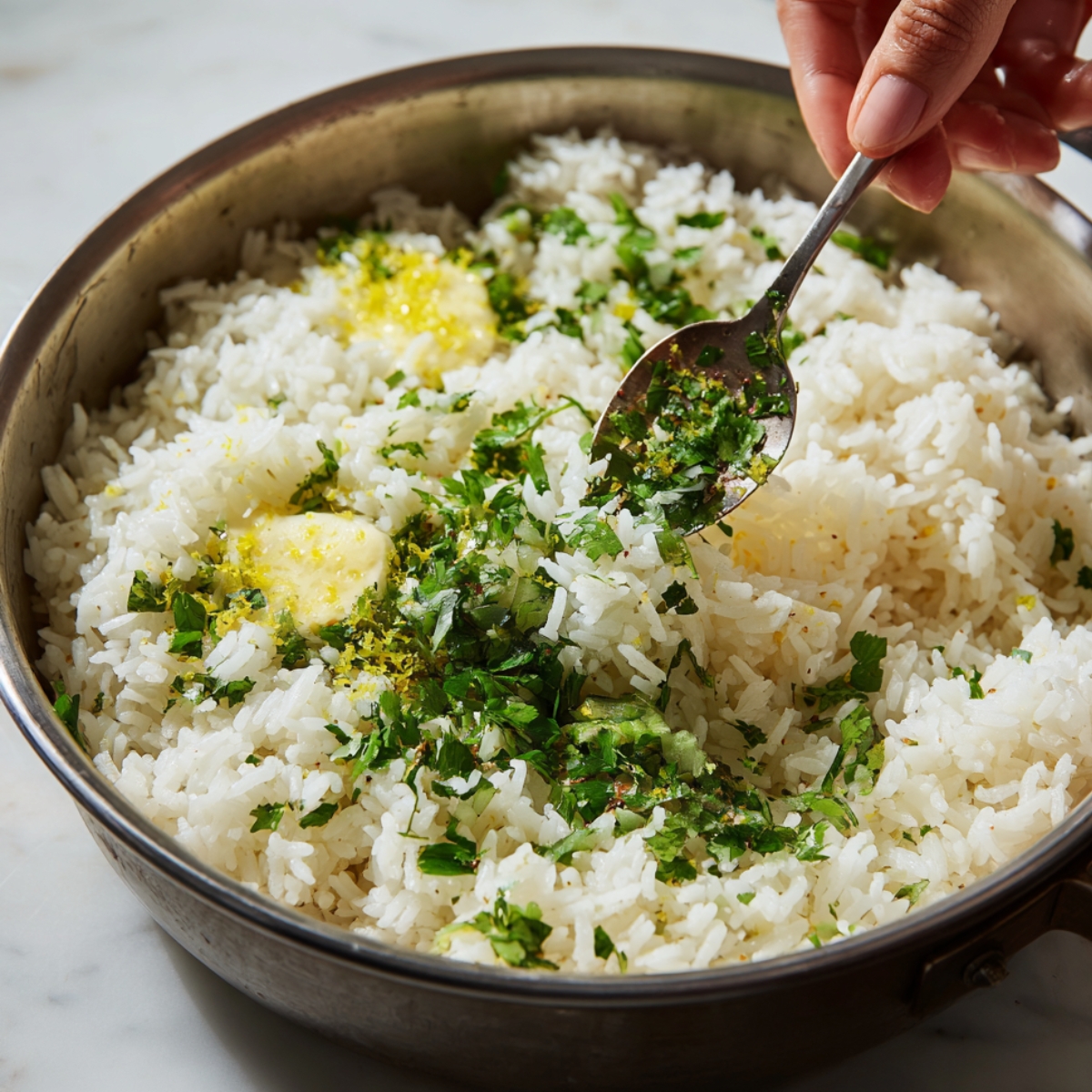 Healthy Cilantro Lime Rice Recipe 12 A hand adds fresh cilantro, lime zest, and butter to a pan of hot cooked white rice, gently mixing the ingredients with a spoon.