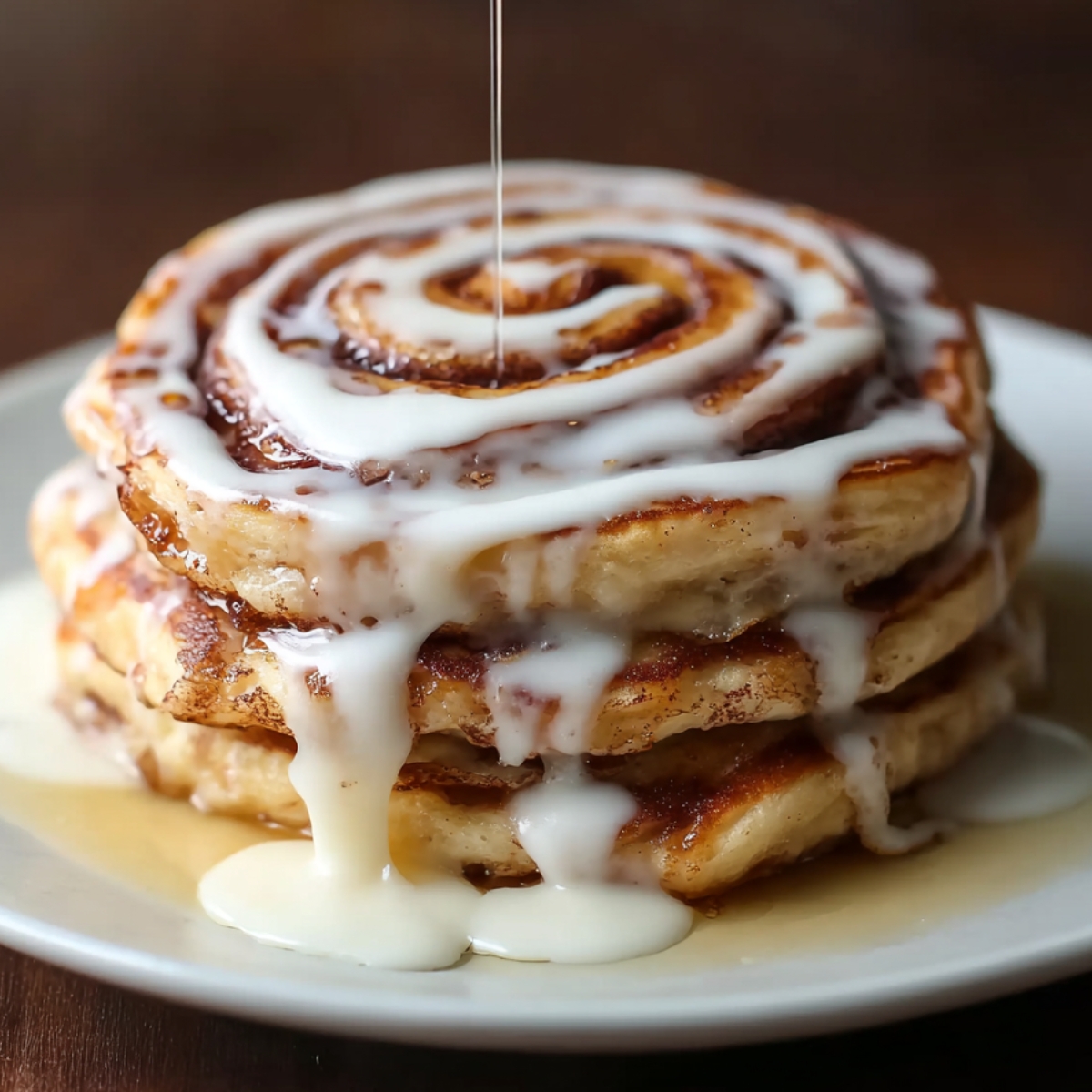 Slice cut from a stack of cinnamon roll pancakes showing the cinnamon swirl inside, topped with dripping glaze.