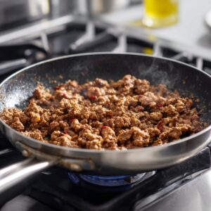 Best Creamy Beef And Shells Recipe 15 Tomato sauce simmering in a stainless steel pan with a wooden spoon lifting some of the sauce.