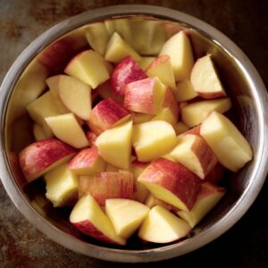 A stainless steel bowl filled with freshly chopped red-skinned apple pieces ready for cooking.