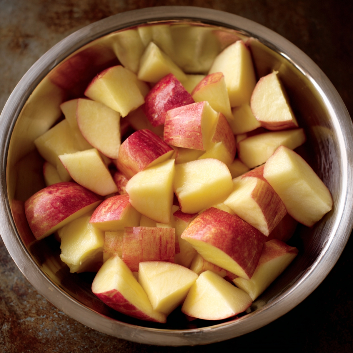A stainless steel bowl filled with freshly chopped red-skinned apple pieces ready for cooking.