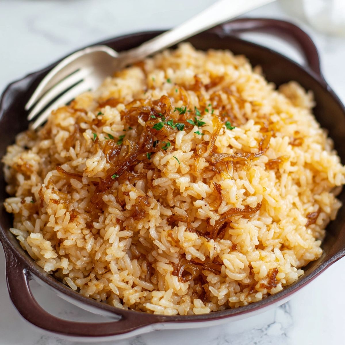 A serving dish filled with French onion butter rice, topped with caramelized onions and sprinkled with chopped parsley.