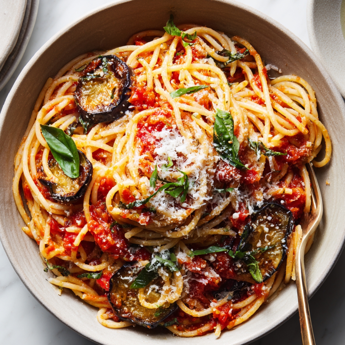 Easy Pasta Alla Norma Recipe 12 Pasta Alla Norma A plate of thick spaghetti coated in rich tomato sauce, sprinkled generously with grated cheese and fresh basil, with a glass of white wine beside it.