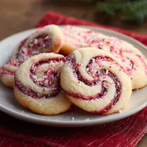 A plate of peppermint swirl cookies coated in sugar, with red and white spiral centers and crushed peppermint pieces sprinkled on top.
