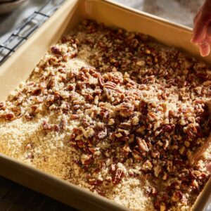 Healthy Possum Pie Recipe In 30 Minutes 15 A baking dish filled with pecan crust mixture made of chopped pecans, flour, butter, and sugar, being pressed and smoothed by hand before baking.