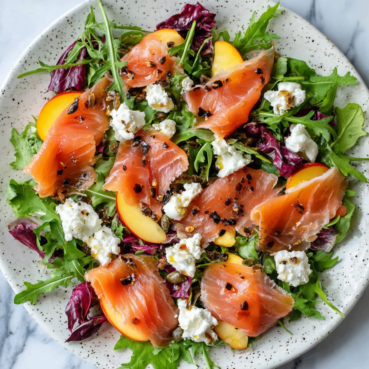 The Best Smoked Salmon Salad Recipe 12 A vibrant smoked salmon salad with mixed greens, peaches, goat cheese, and crushed pepper, arranged beautifully on a speckled ceramic plate.