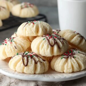 Healthy Whipped Shortbread Cookies Recipe 18 "Close-up of tender whipped shortbread cookies topped with red, green, and white holiday sprinkles, showing their delicate, crumbly texture on a decorative plate."