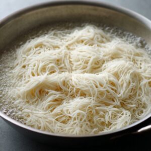 Rice noodles boiling in a pan of hot water, softening into loose, white strands.