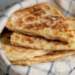 Scottish Tattie Scones A fresh stack of golden Scottish tattie scones wrapped in a cloth, showing their soft and fluffy interior with a crisp exterior.
