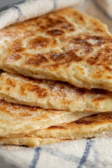 The Best Scottish Tattie Scones Recipe (Just 3 Ingredients!) 2 Scottish Tattie Scones A fresh stack of golden Scottish tattie scones wrapped in a cloth, showing their soft and fluffy interior with a crisp exterior.