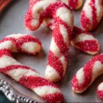 Candy Cane Cookie A close-up of freshly baked candy cane-shaped cookies on a tray, glistening with sparkling sugar.